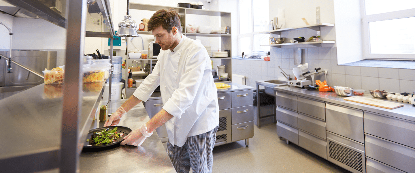 A man in a chefs jacket working in a kitchen preparing a salad
