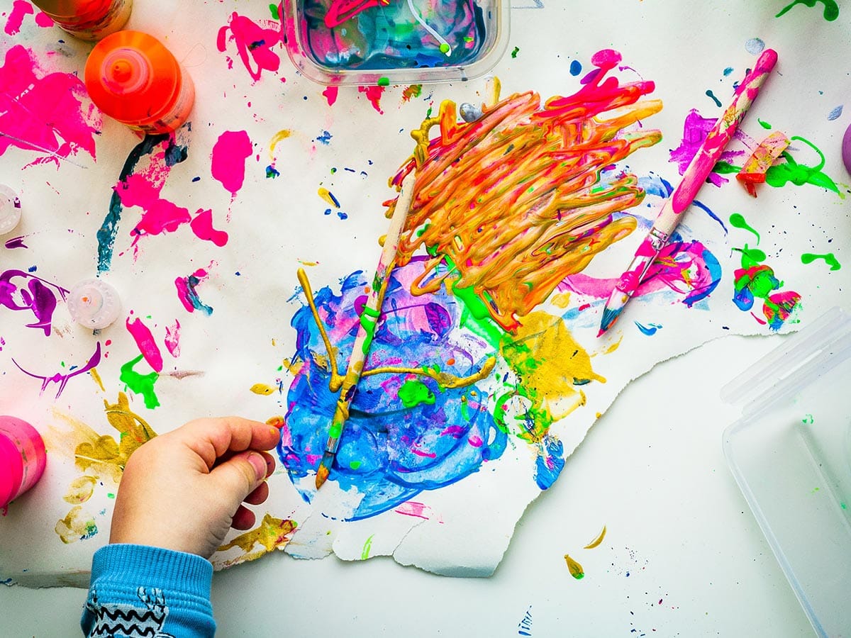 Messy paints on an artists canvas with a child's hand in the foreground