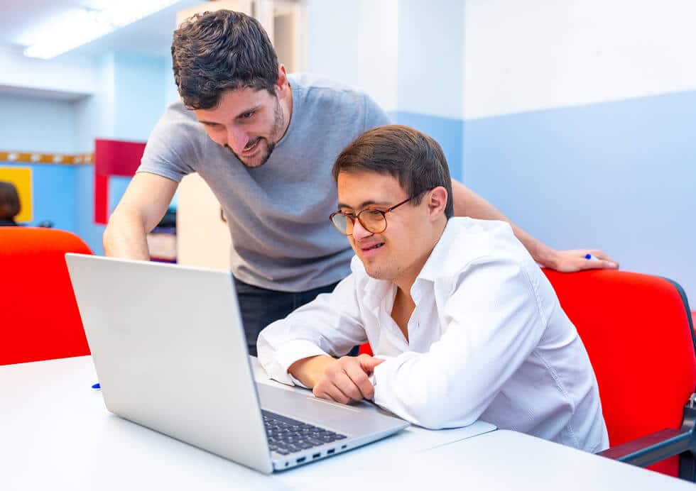 Your man using a laptop sat at a desk with their support worker who is helping them with something on the computer.