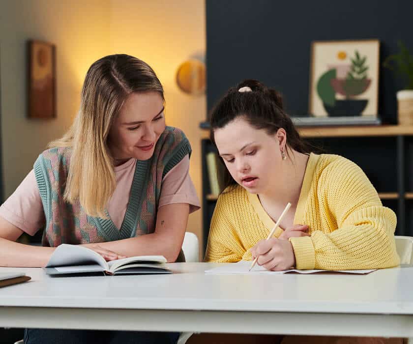 Young woman sat at a desk writing, whilst getting support from a social worker.