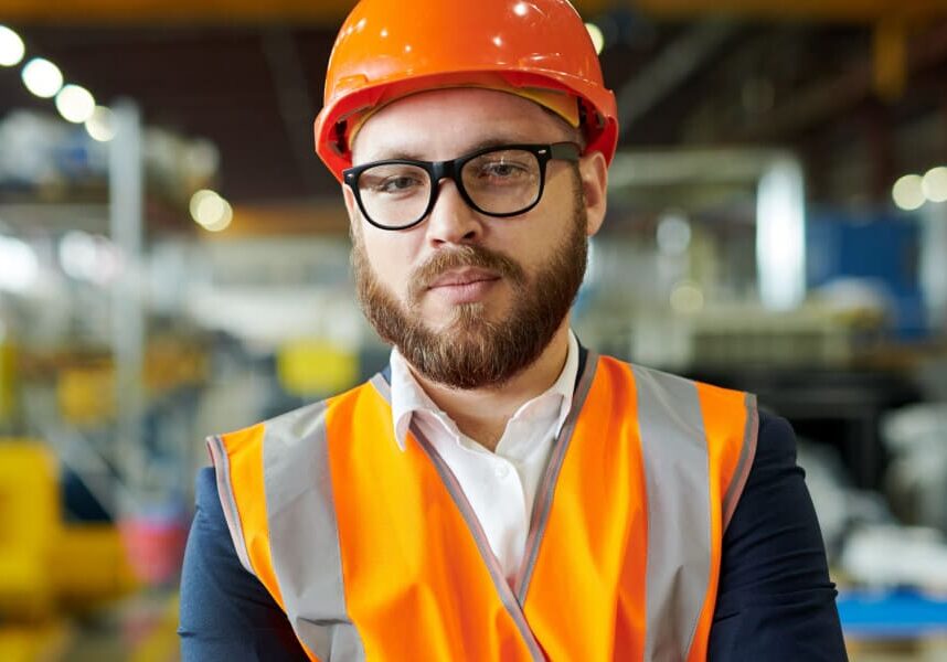 A male engineering worker in an orange hard hat and high visibility vest in a factory