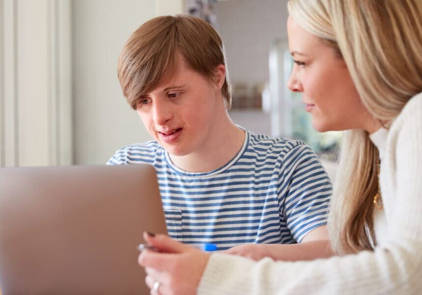 A young man with down syndrome using a computer with support from an employment navigator
