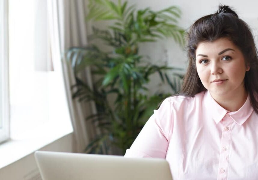 A girl in a modern lounge in pink shirt using a laptop